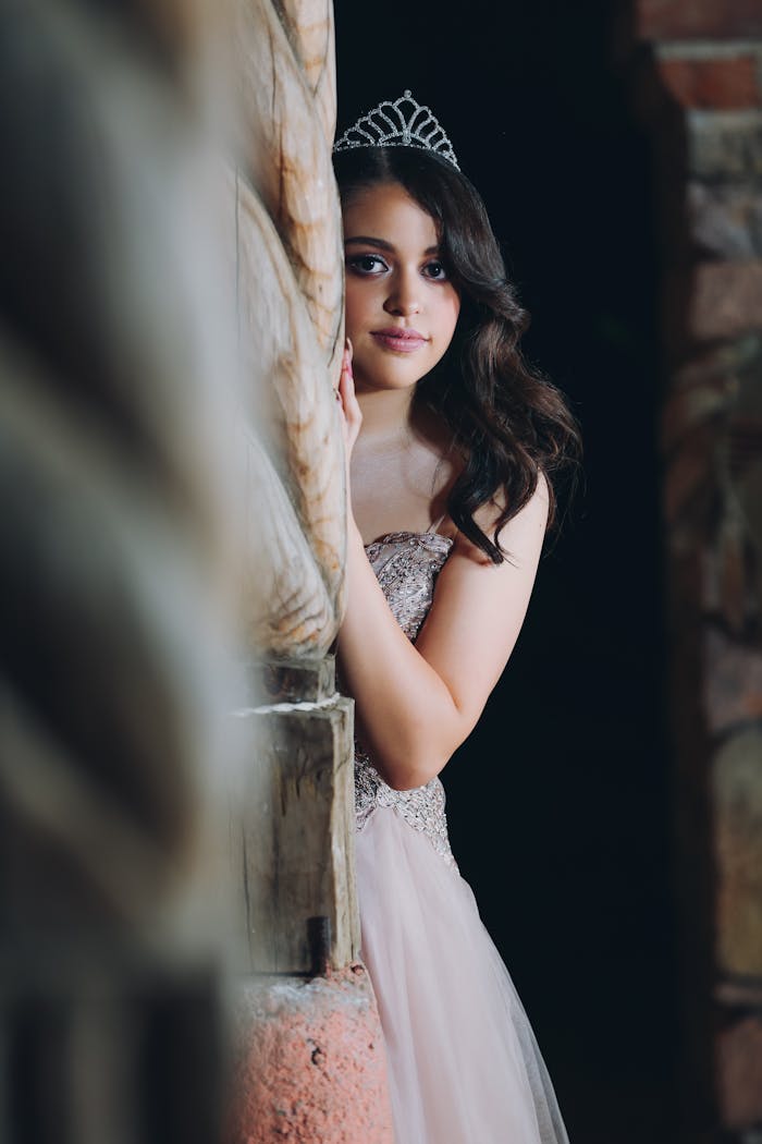 Beautiful teen girl in gown, posing with tiara. Capture of elegance and style.